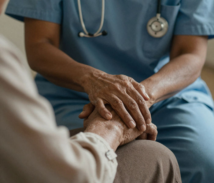 A caregiver in scrubs gently holding an older person's hands